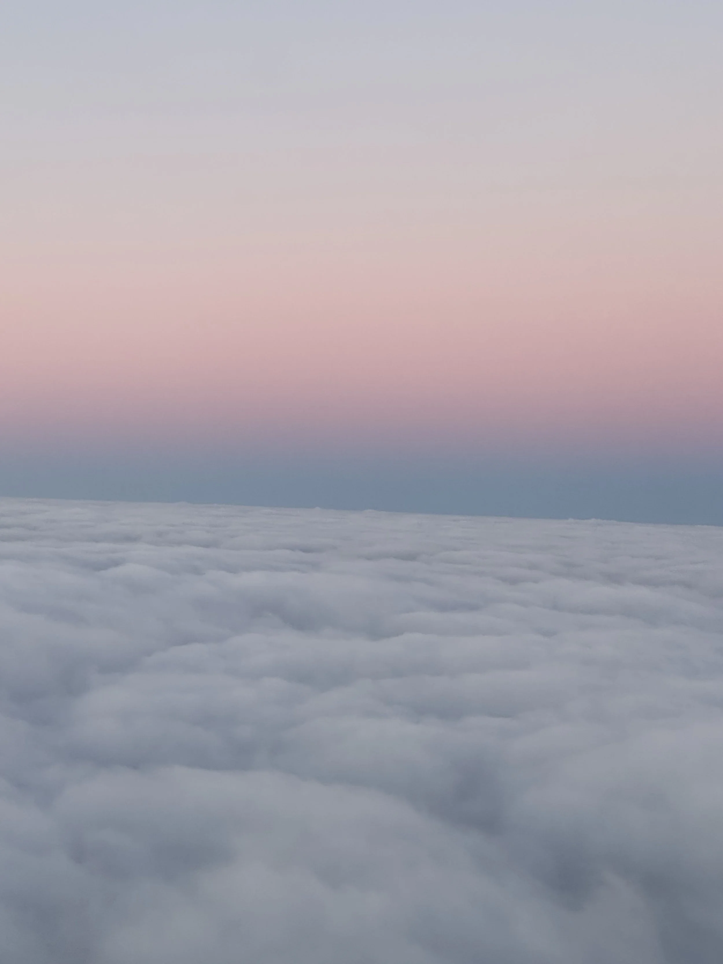 Clouds seen from above with a pastel-colored sky in the background.