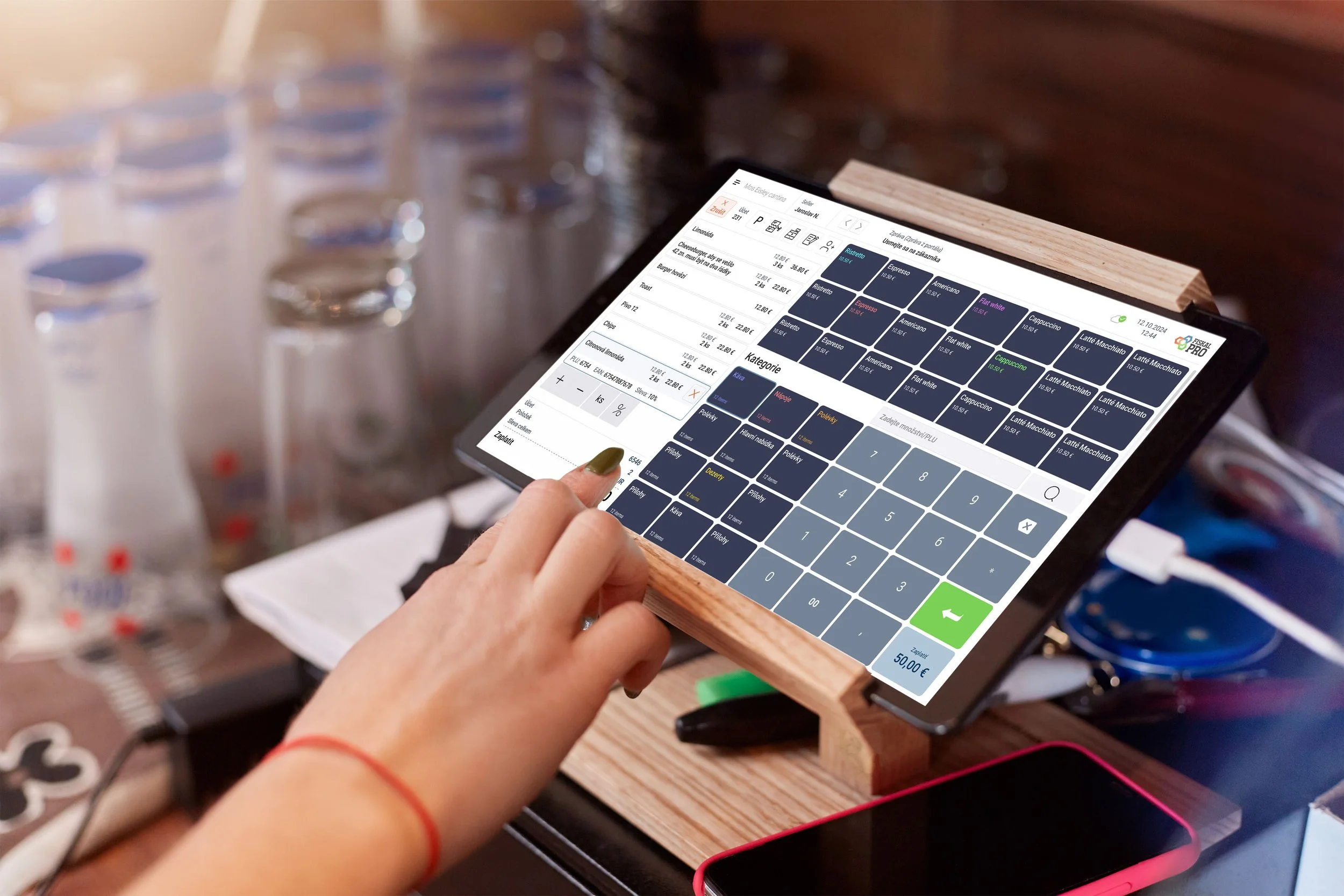 A person using a tablet with a point-of-sale app on a wooden stand, during a transaction at a cafe or shop.