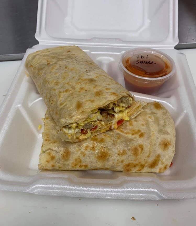 A takeout box with a partially unwrapped breakfast burrito and a small container of hot sauce.