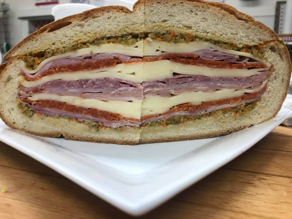 Cross-section of a sandwich with layers of ham, cheese, roast beef, and other deli meats inside a hoagie bun, served on a white plate.