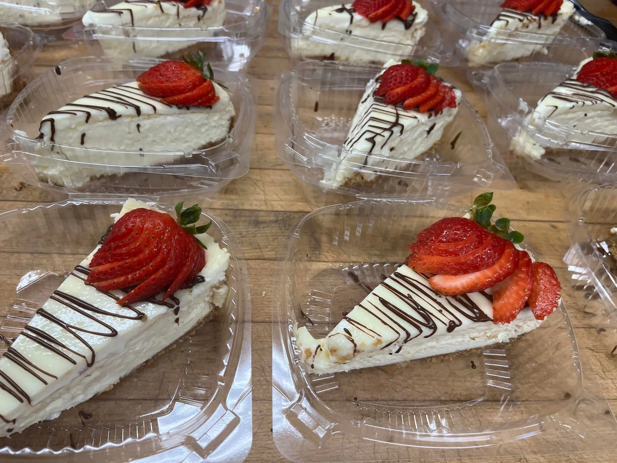 Slices of cheesecake topped with sliced strawberries and a drizzle of chocolate, on clear plastic trays.