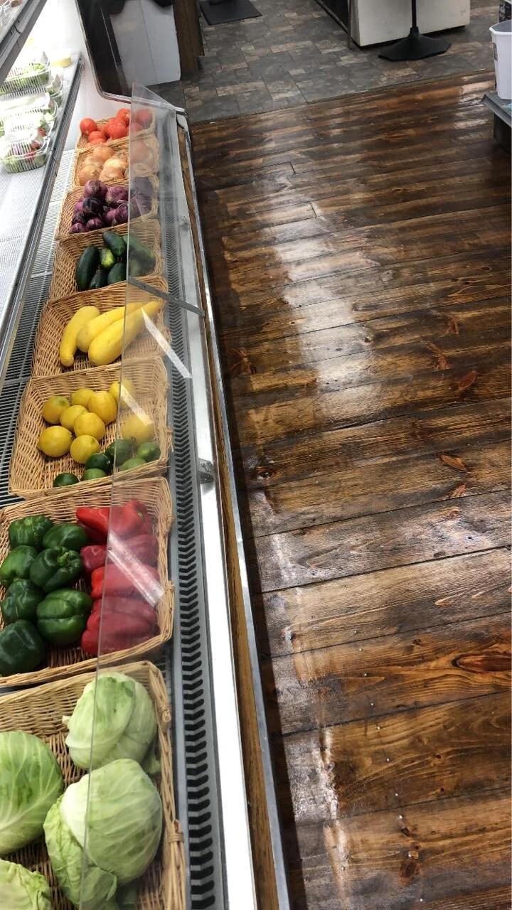 Display case with fresh vegetables including green bell peppers, red bell peppers, lettuce, lemons, zucchini, red onions, tomatoes, and cucumbers in a grocery store.