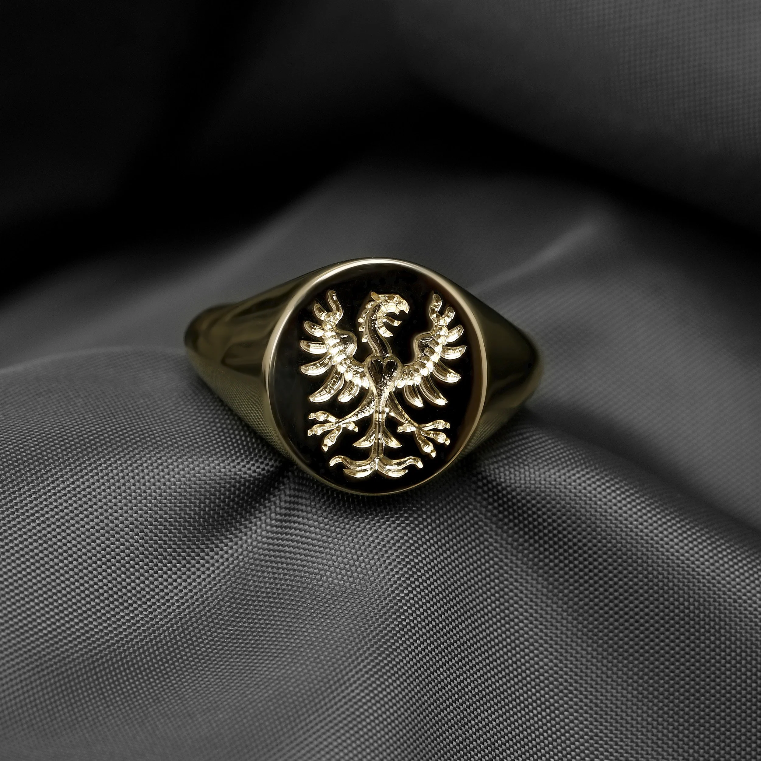 Gold signet ring with a crest of an eagle on a dark fabric background.