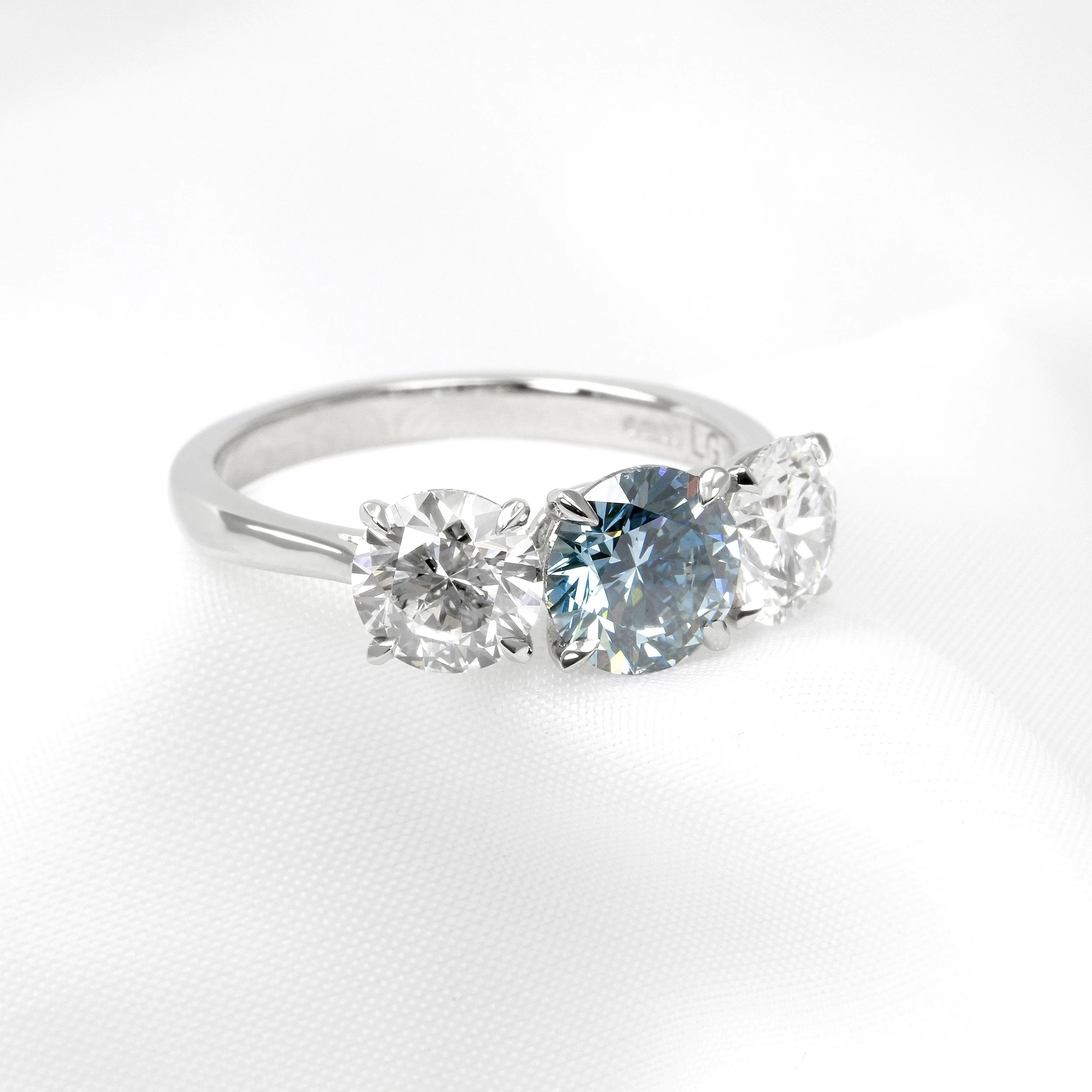  Timothy Roe Laboratory-Grown Diamond Three Stone Ring in Platinum. Three round brilliant cut laboratory-grown diamonds centre: 1.41ct fancy vivid blue. Sides: 1.00ct, D, VVS2.   Blue diamonds can sometimes have a steely silvery undertone similar to Montana Sapphires and denim jeans.  