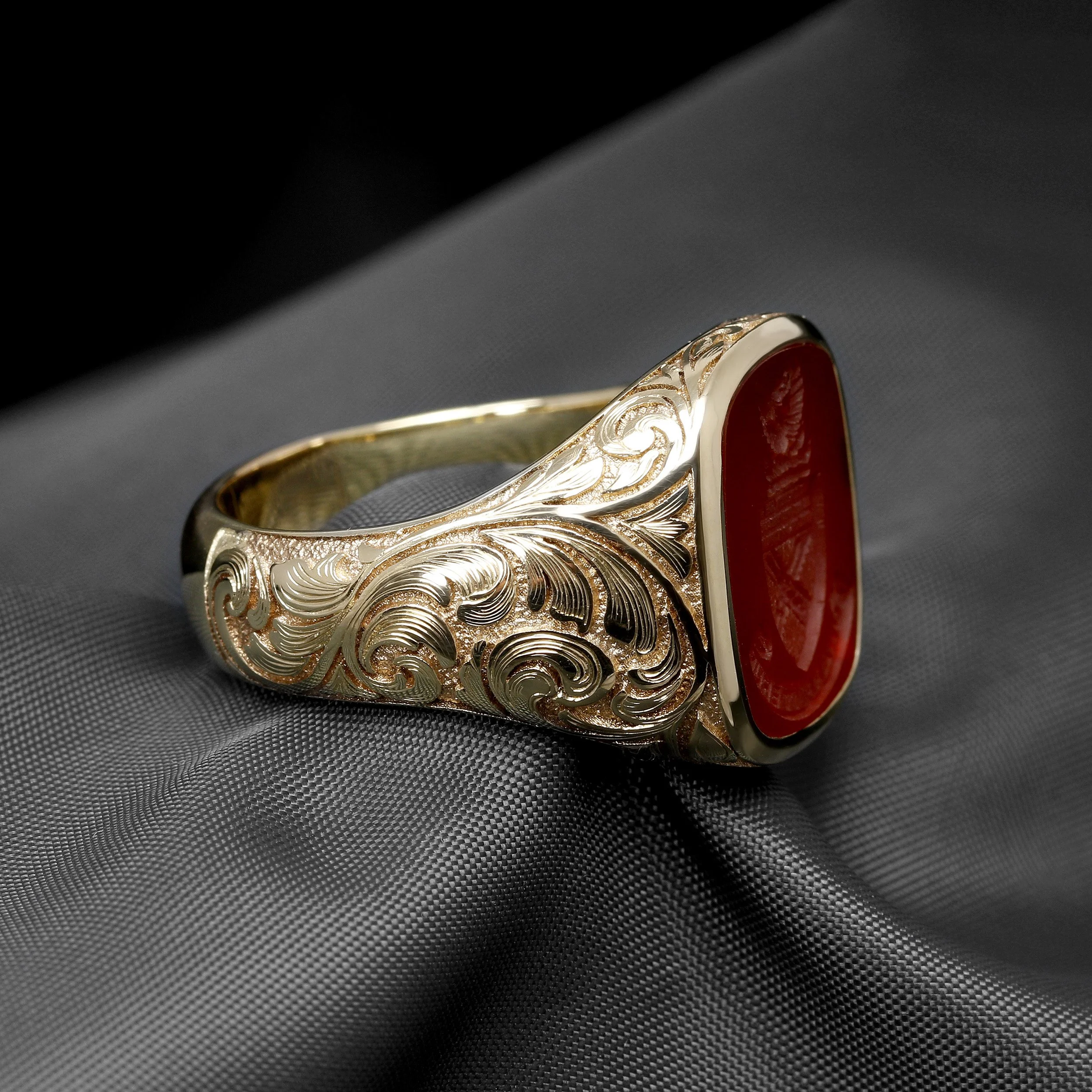 Gold signet ring with intricate engraved patterns and a large red oval carnelian set in the center.