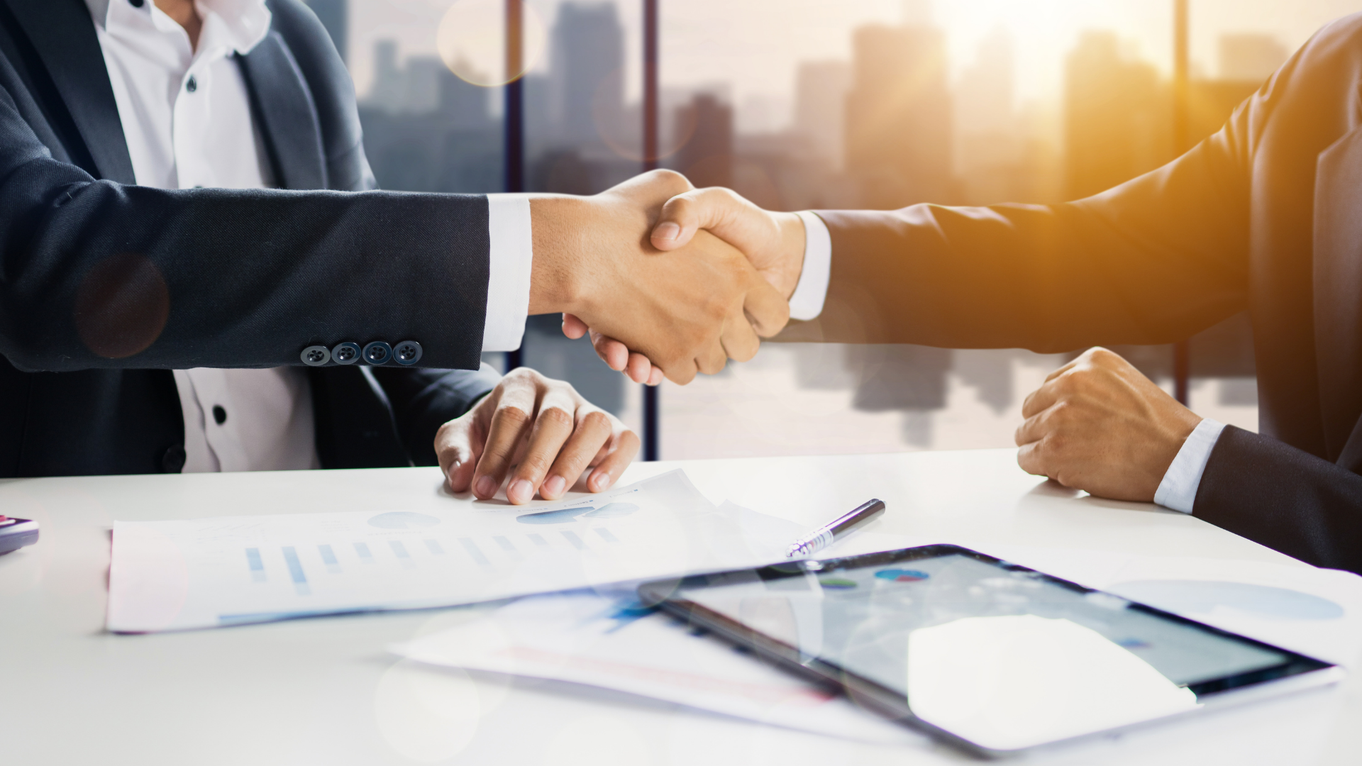Two business people seated at a conference table shaking hands.