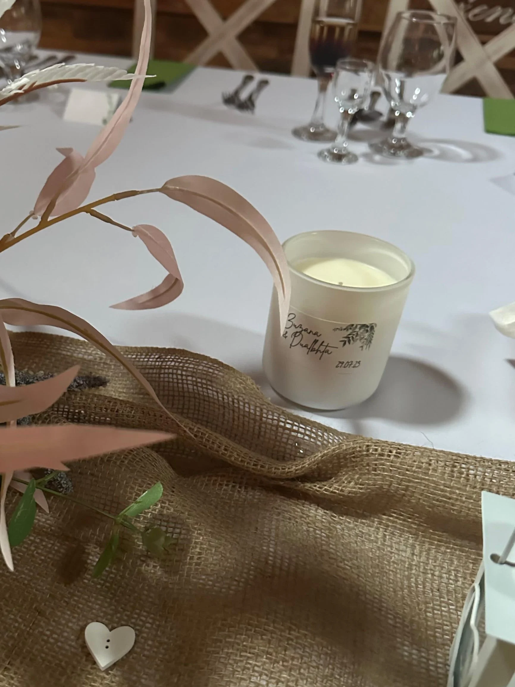 Table setting with white candle and glasses on burlap surface