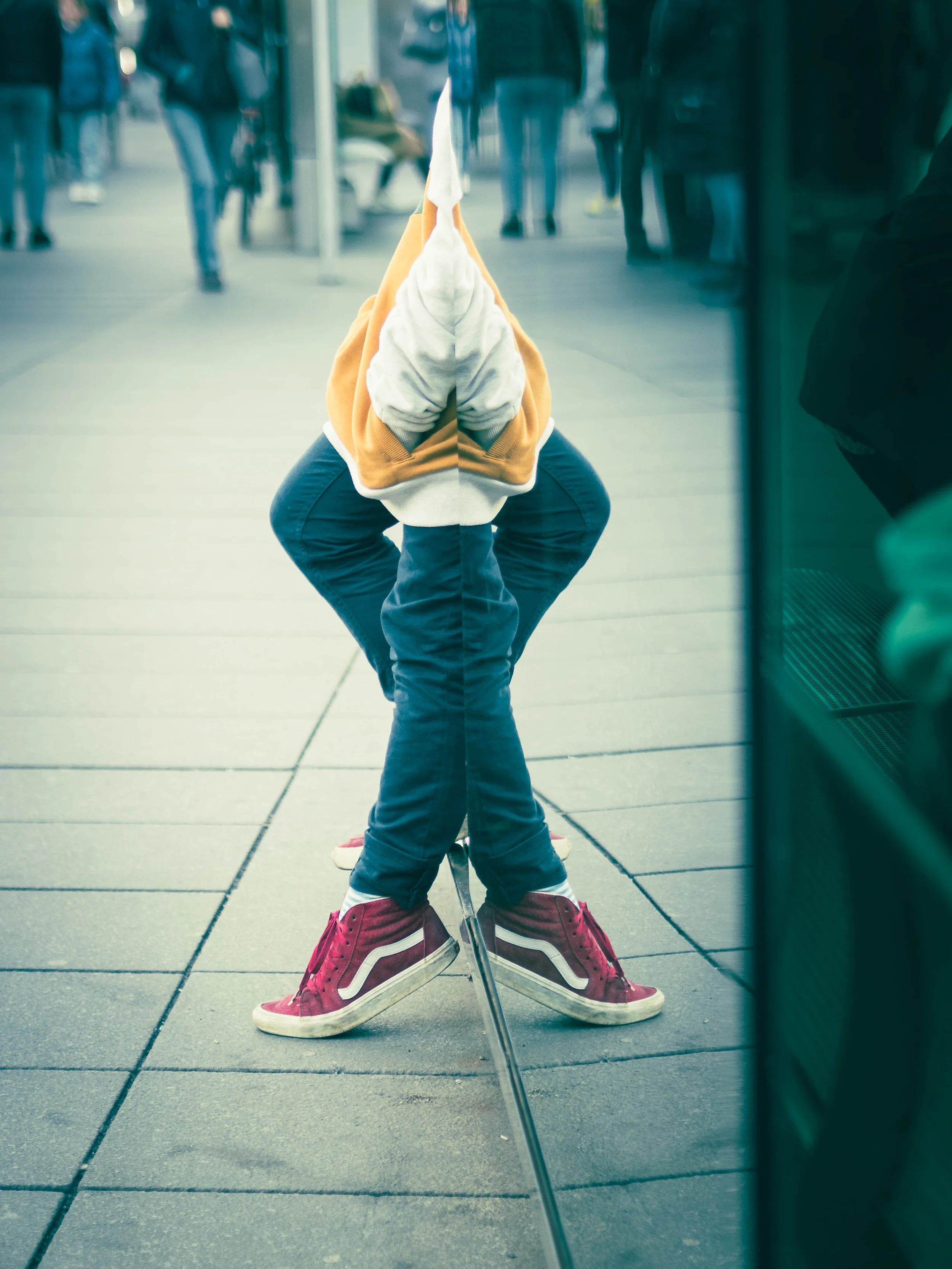 Reflexion eines Menschen, der sich im Schaufenster betrachtet, mit dem Gesicht in den Händen, auf dem Gehweg einer Stadt.