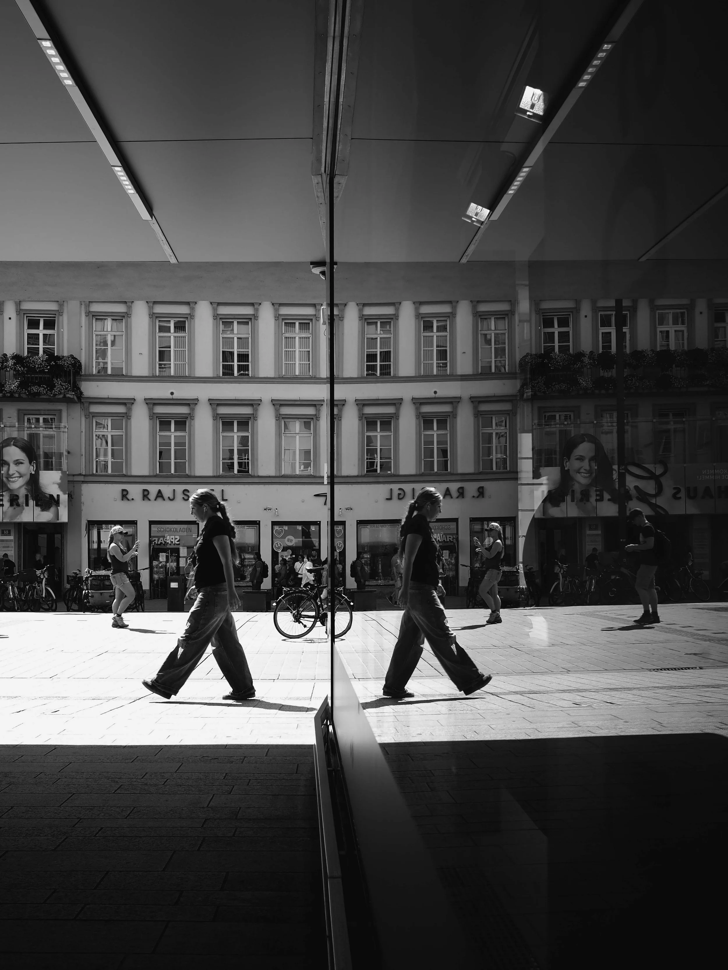 Reflexion einer Stadtstraße mit mehreren Fußgängern, Fahrrad und Geschäften in einer Glasscheibe, schwarz-weiß