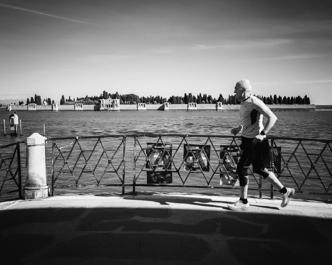 Ein Mann joggt entlang eines Wasserufers, im Hintergrund ist eine Burg oder Festung auf einer Insel im Wasser sichtbar.