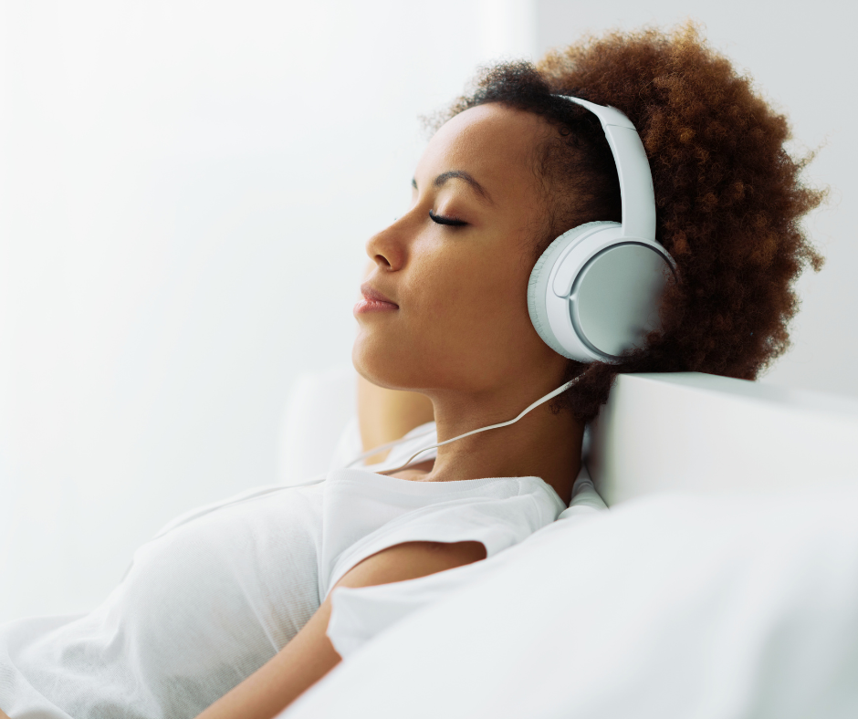 A young woman with curly hair wearing headphones and relaxing with her eyes closed.