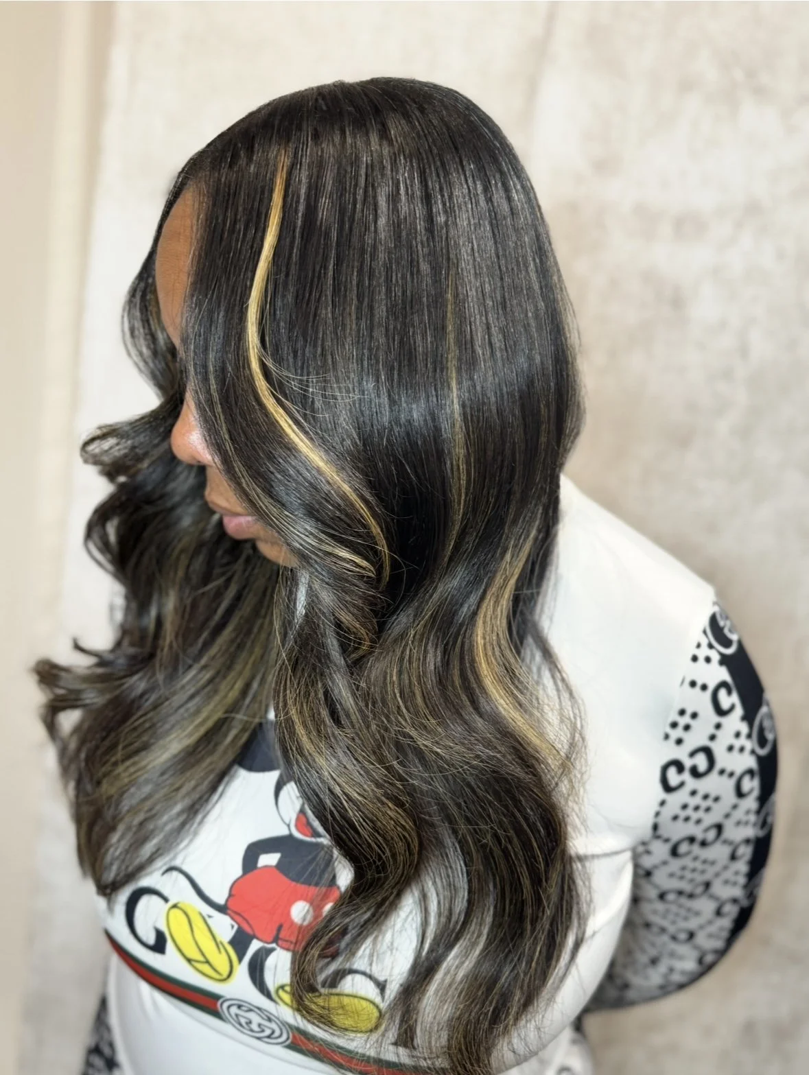 Side view of a woman with long, wavy black hair with blonde highlights.