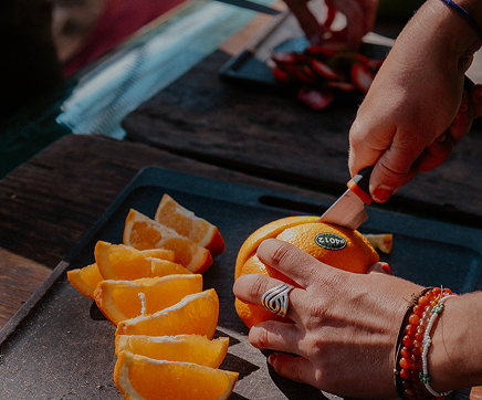 Person slicing a fresh orange on a dark tray, with orange wedges nearby.