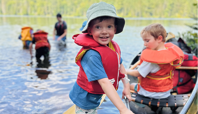 Children enjoying a boat trip on a river, wearing life jackets and outdoor gear.