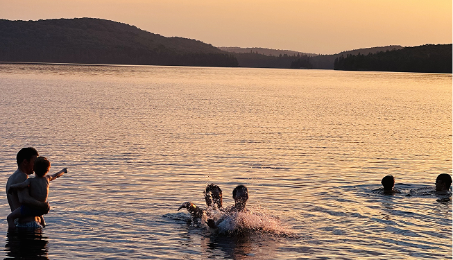 Kids swimming and playing in a lake during sunset with hills in the background.