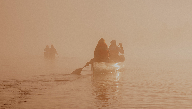 Several people in a boat on foggy water.