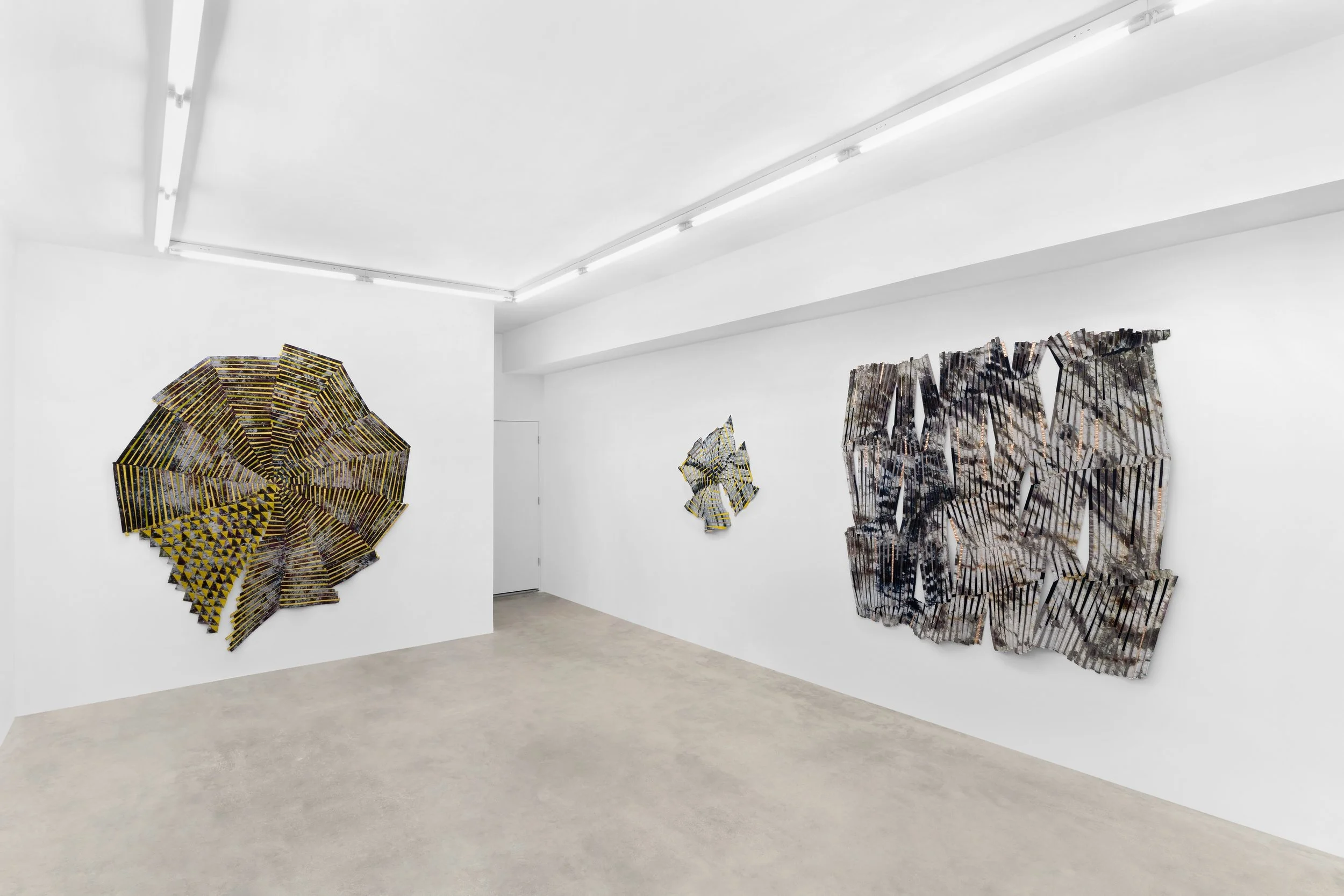 Baker–Hall Gallery - Regina Durante Jestrow: 'Everything Mixing Always' installation view of geometric abstract art quilts made from hand-dyed and found textiles arranged in geometric stripes and triangle patterns in an art gallery with white walls.