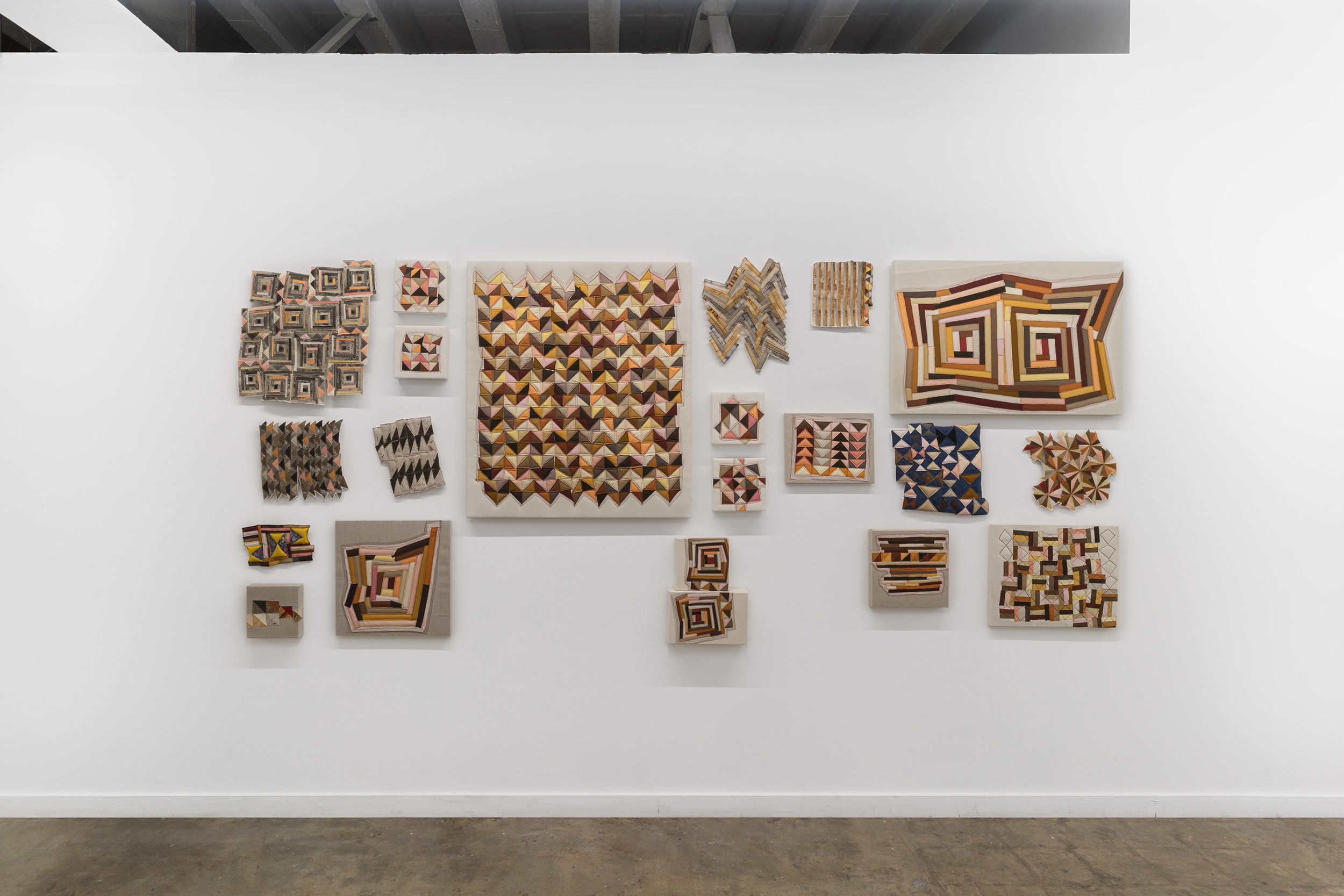 Wall display of various geometric abstract art pieces in different sizes and shapes with earthy tones and patterns.