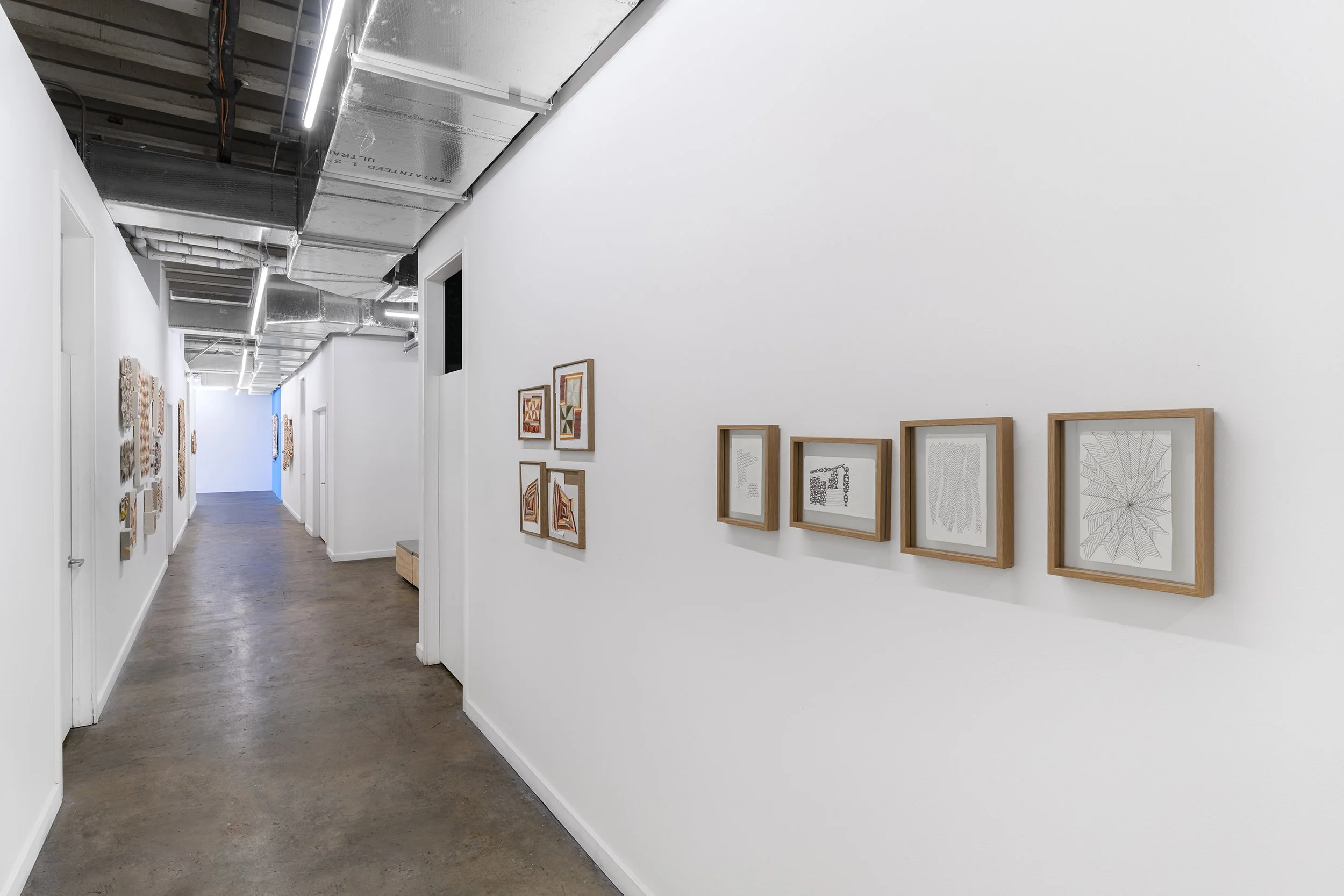 Art gallery corridor with abstract framed artwork on white walls and ceiling with exposed ductwork.