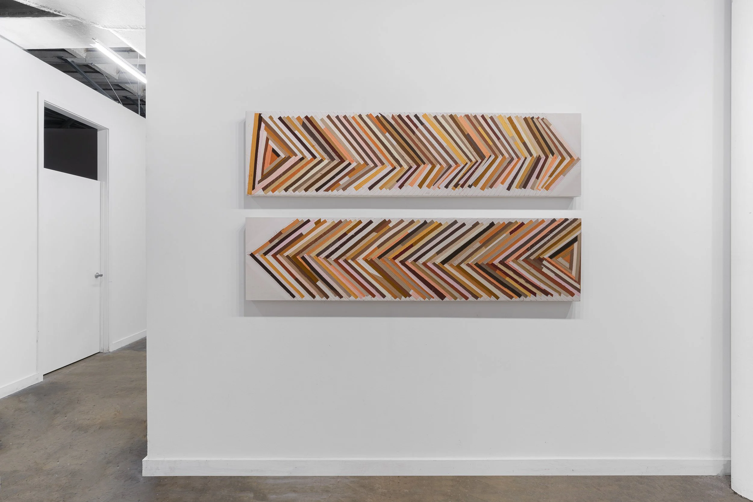 Two abstract geometric paintings with arrow shapes and parallel lines in shades of brown, pink, orange, red, and black on a white gallery wall.