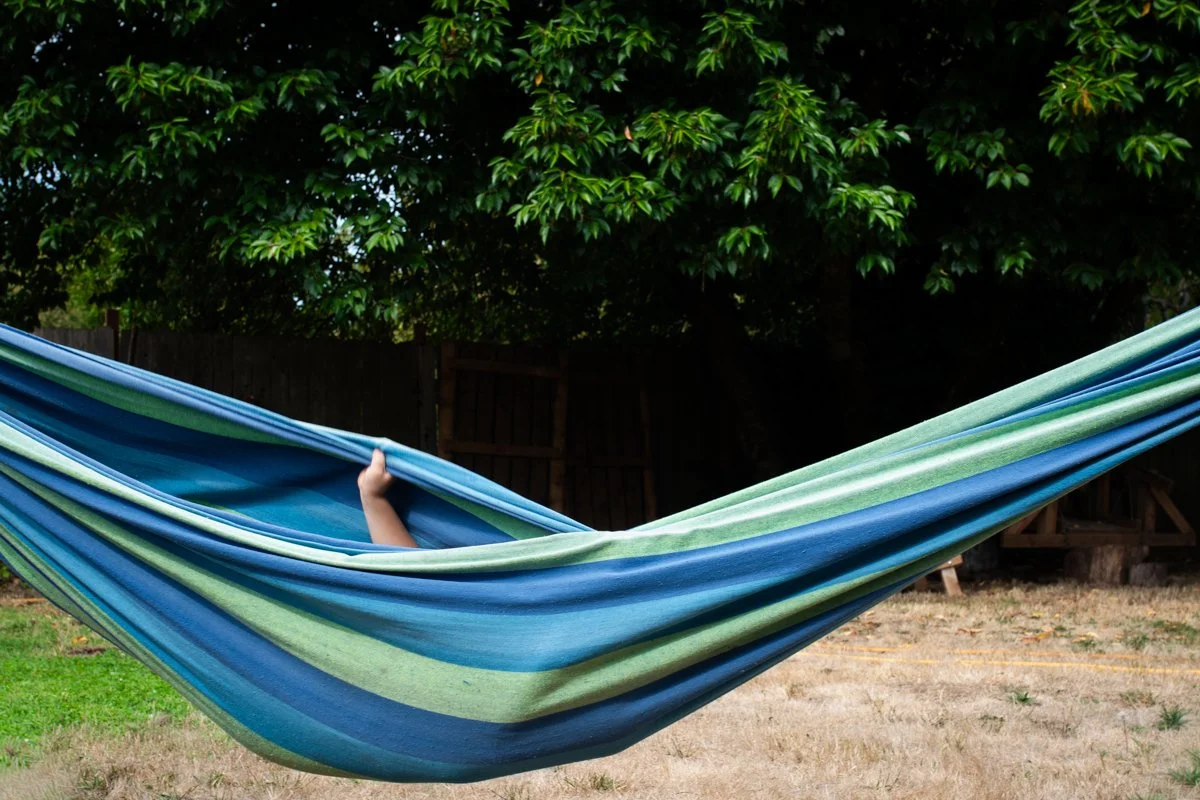 Kid playing in the hammock in the backyard during a day in the life session in Portland OR. No faces shown. Documentary candid photojournalist photography.