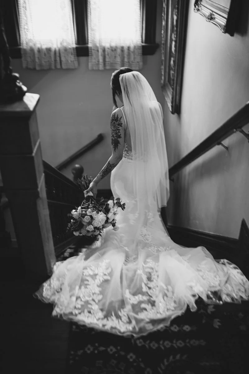 The Belle Victorian Mansion Wedding Photographer Portland, a black and white photograph of a bride going down the stairs. A wedding, elopements and events documentary photographer.