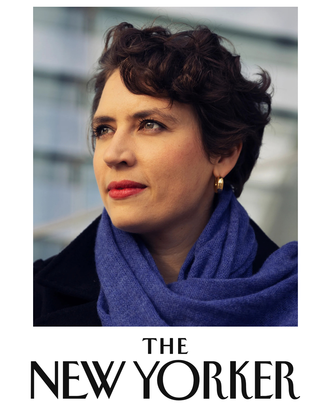 Close-up of a woman with short, curly dark hair, wearing gold hoop earrings, a blue scarf, and a dark coat, looking thoughtfully to the side with a blurred modern building in the background.