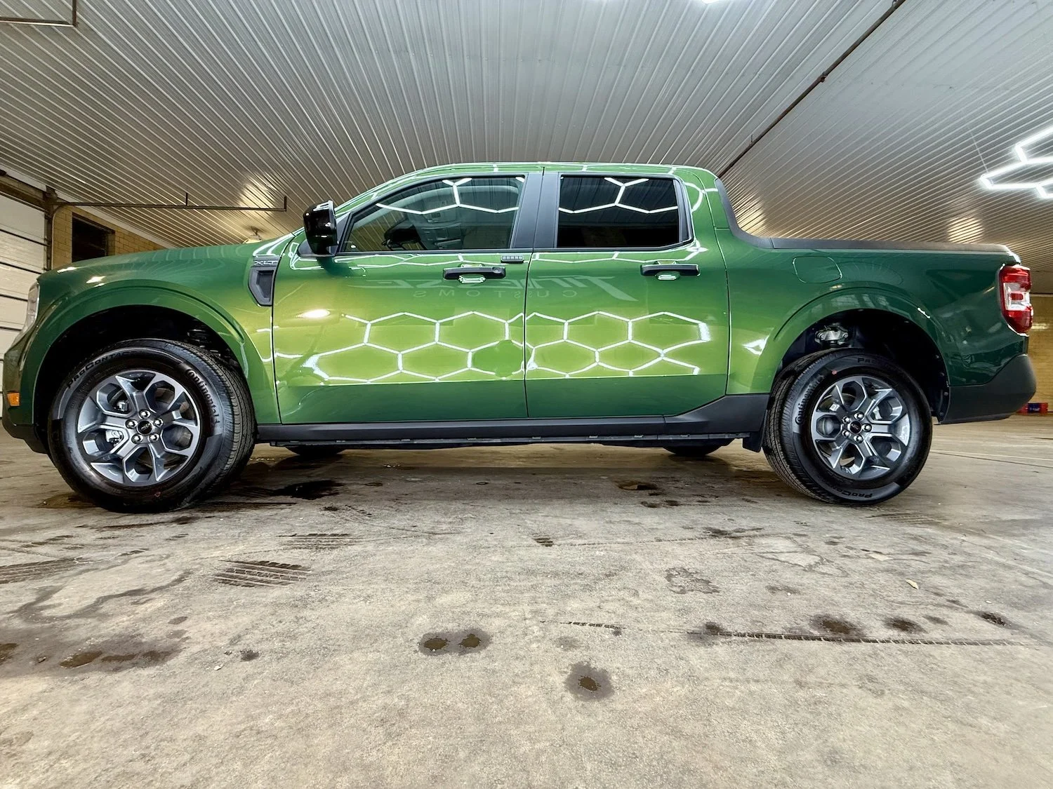 Green pickup truck parked indoors with hexagonal pattern reflection on its side