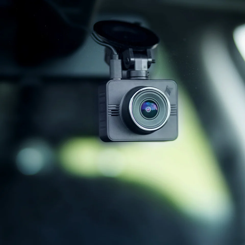 Close-up of a dashboard camera mounted inside a vehicle with a blurred green background.