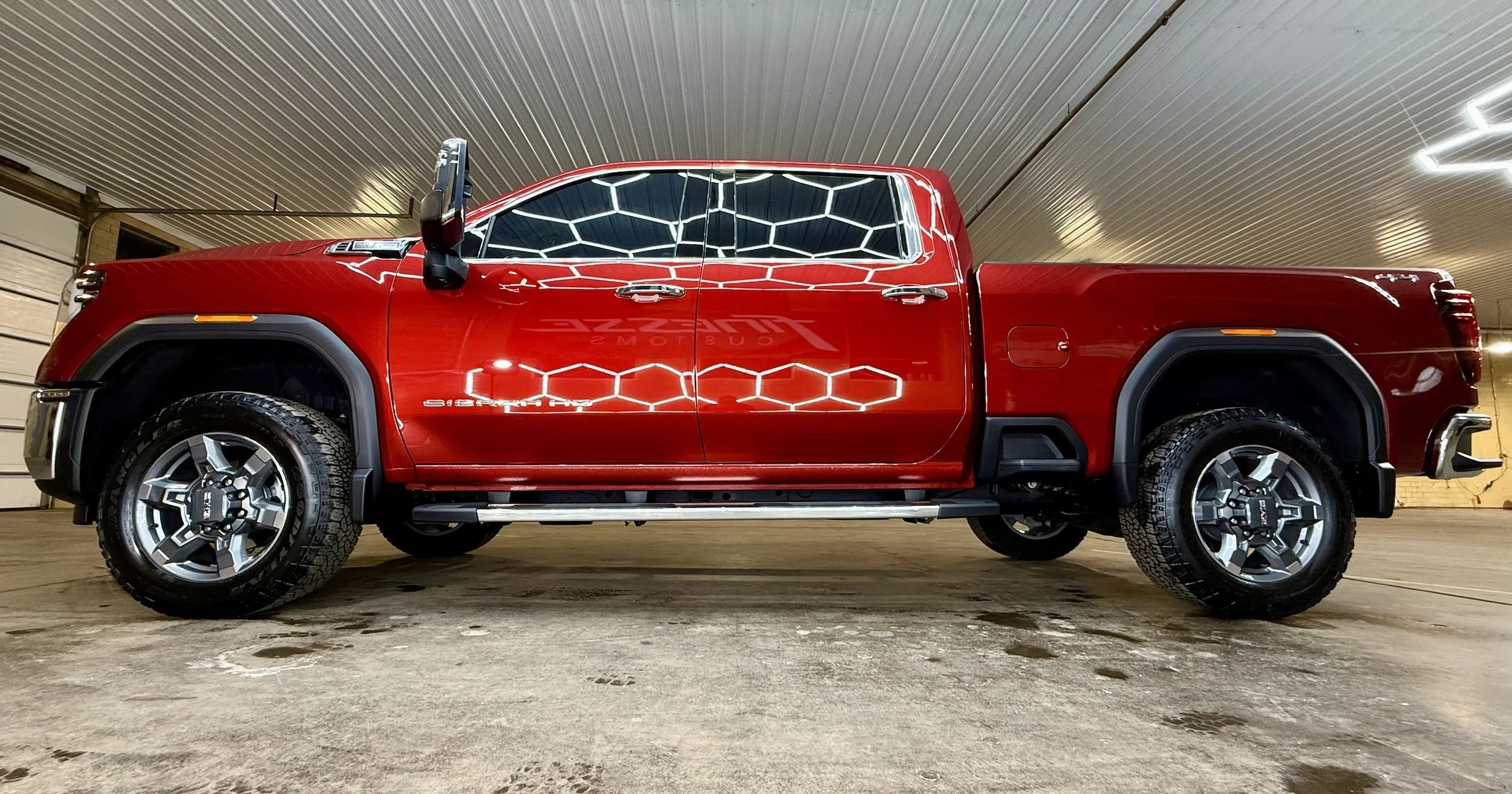 A red GMC Sierra HD pickup truck parked in an indoor garage, viewed from the side.