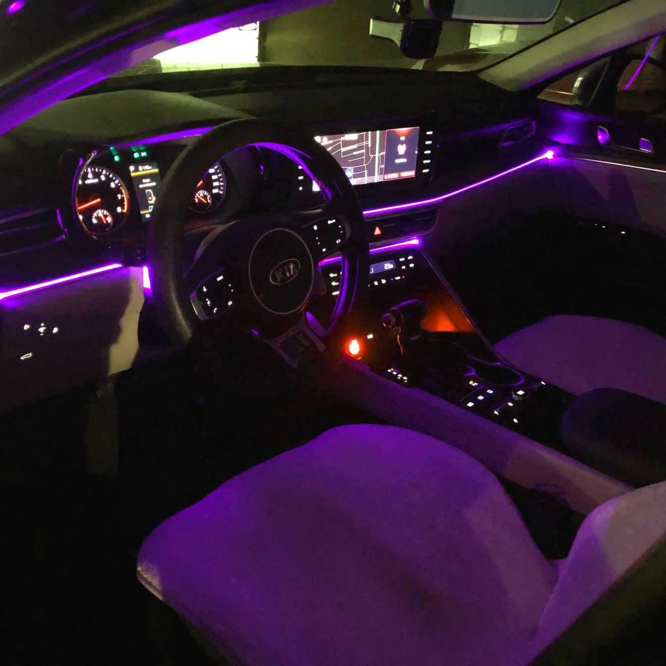 Interior of a Kia car at night with purple ambient lighting, showing the steering wheel, dashboard, and center console.