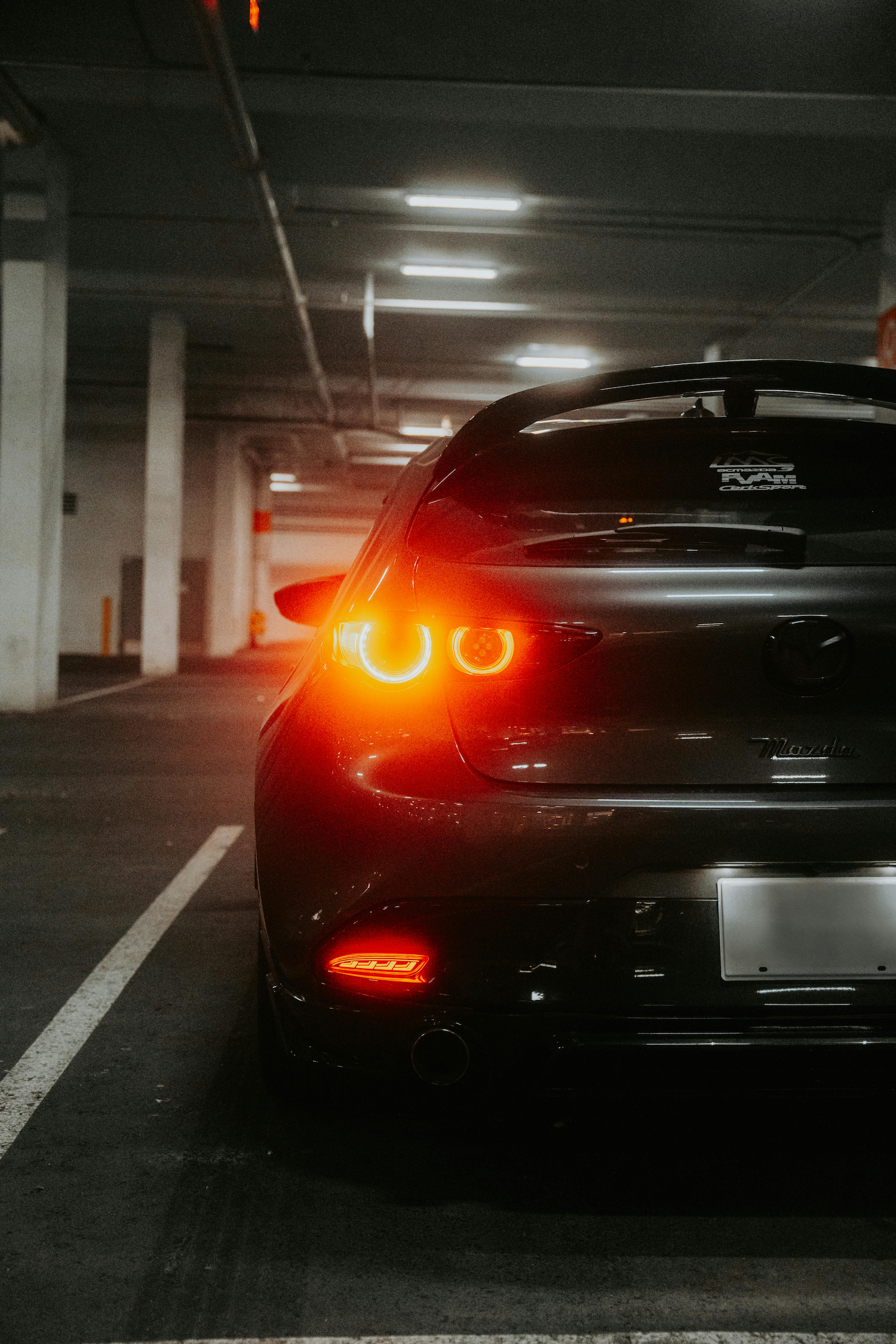Rear view of a dark gray Mazda sports car with illuminated taillights parked in an underground parking garage.