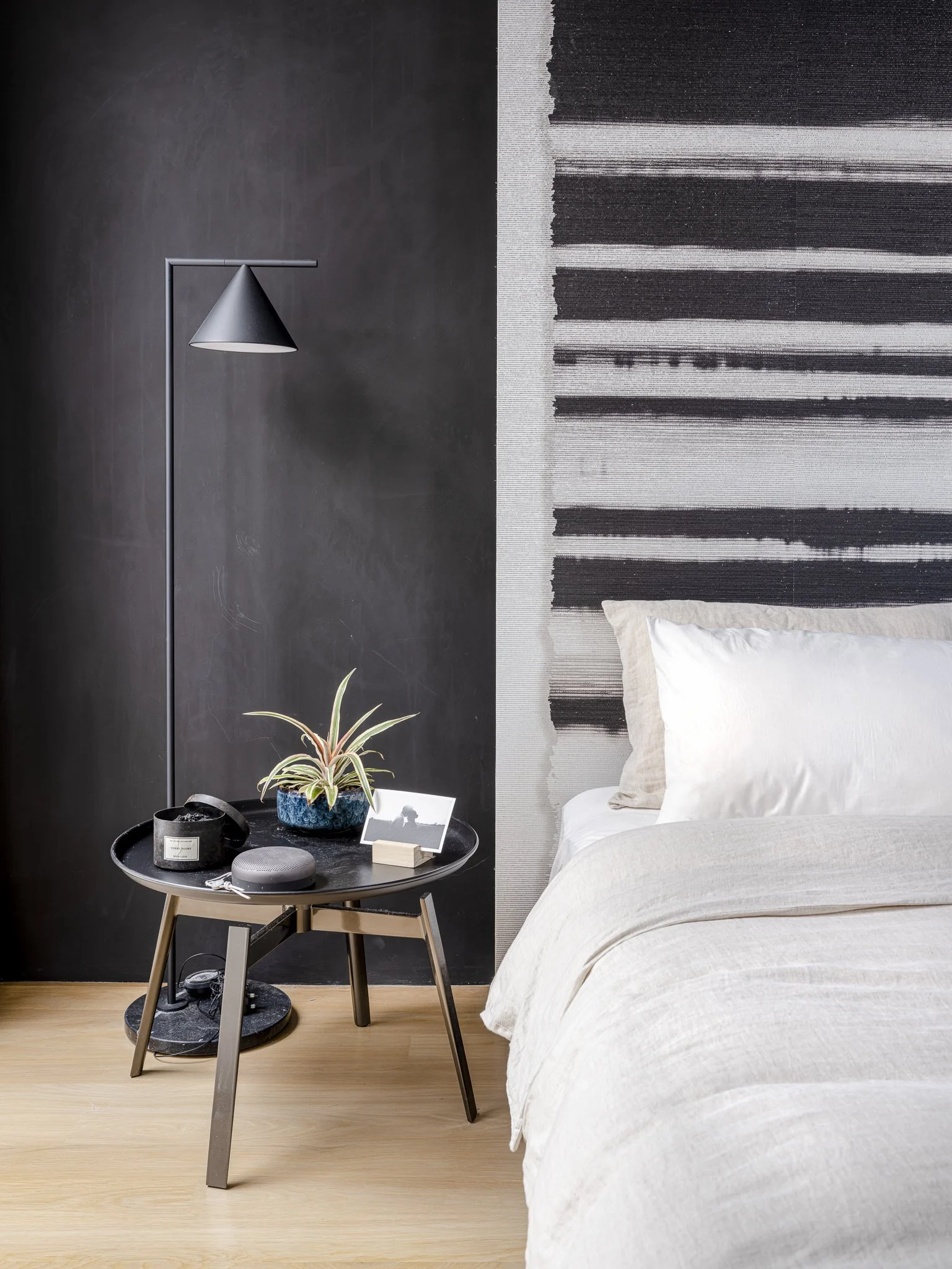 accessories on an end table next to a white bed, with a feature wallpaper as a backdrop