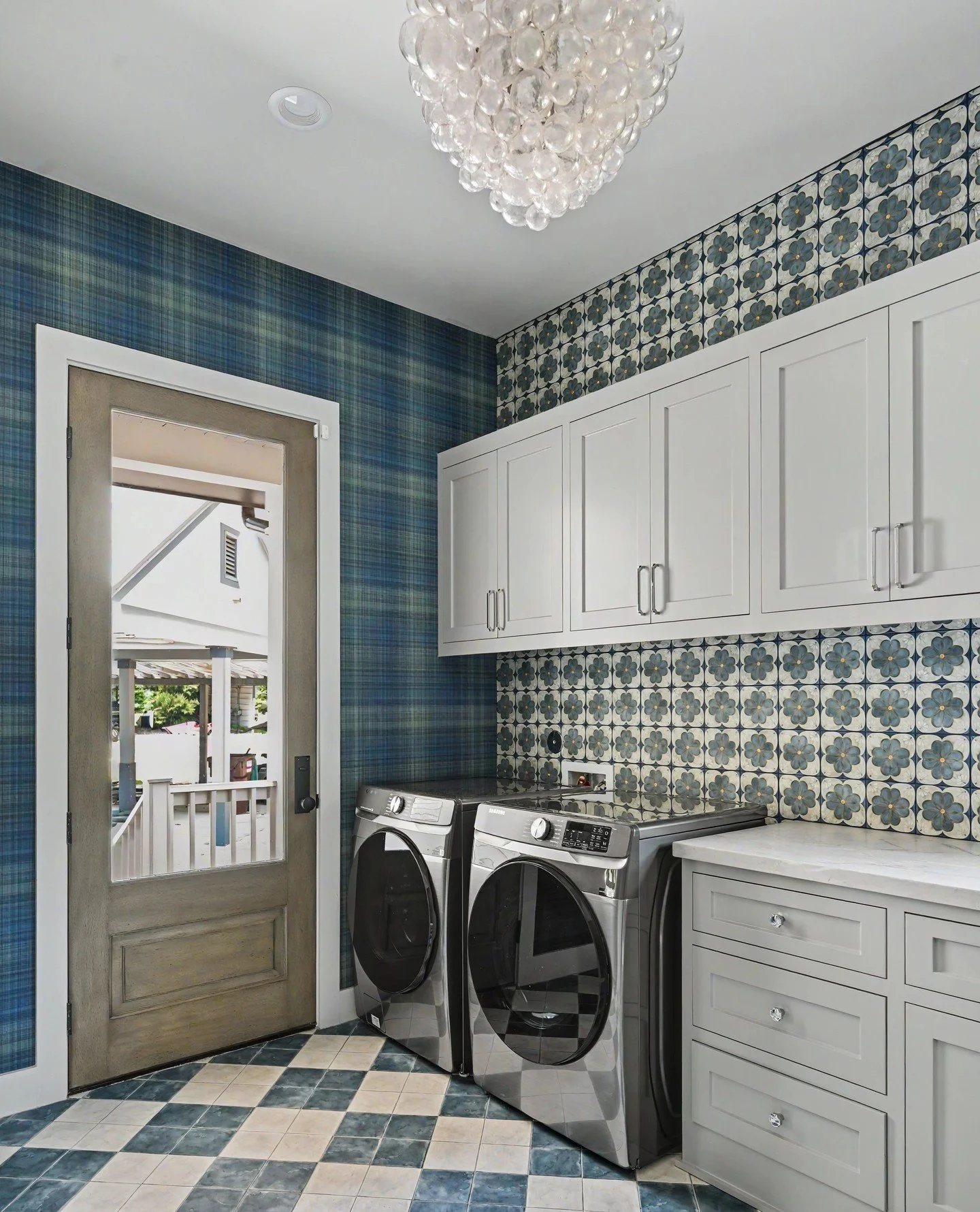 Pattern, but make it polished. ✨ The Visual Comfort bubble chandelier adds a sculptural touch overhead, while the playful mix of plaid wallpaper, floral backsplash, and checkerboard tile creates a laundry room with layers of personality and charm.⁠
⁠