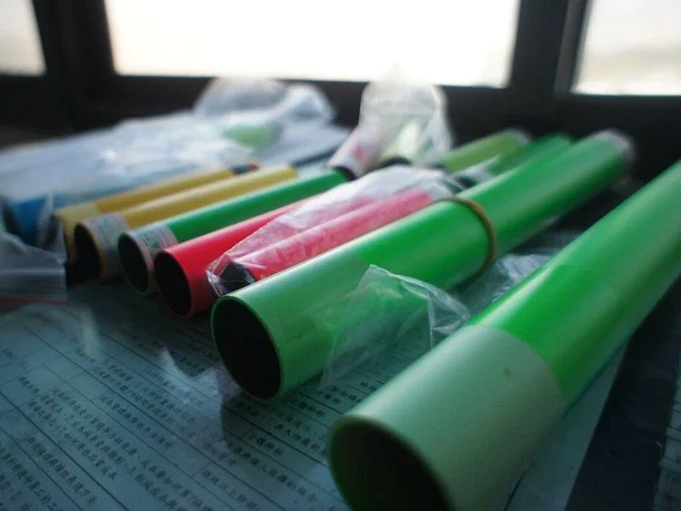 Multiple colored plastic tubes, including green and red, on top of a document with Chinese text, near a window.