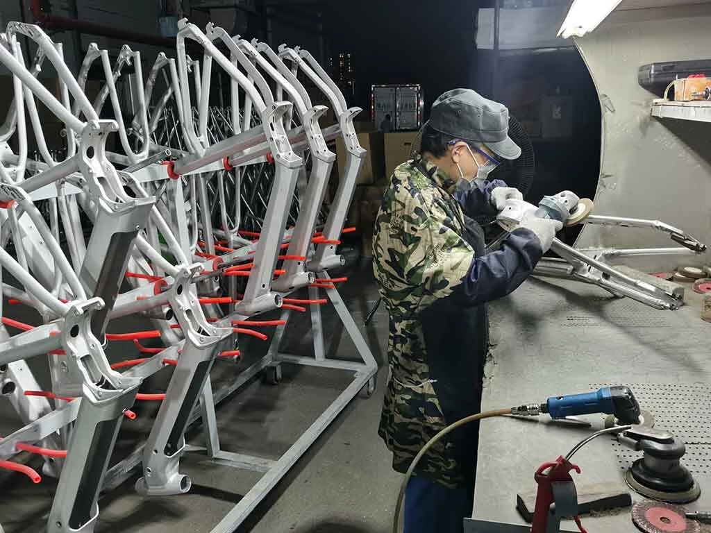 Close-up of machinery with a bicycle wheel being tested or assembled, featuring various metal parts, bolts, and sensors in an industrial setting.
