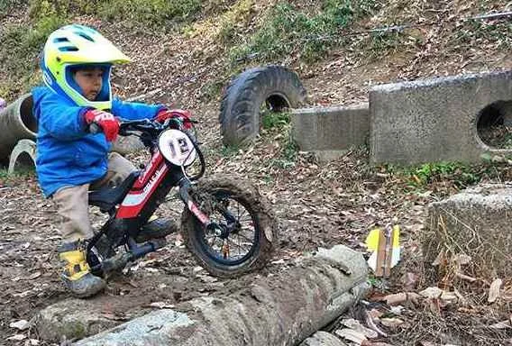 Young boy wearing a helmet riding a mountain bike on a dirt trail with tires and obstacles.