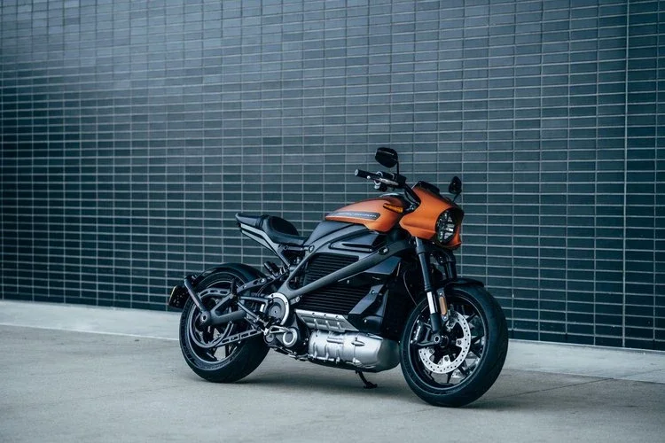 An orange and black Harley Davidson motorcycle parked on a concrete surface in front of a black tiled wall.