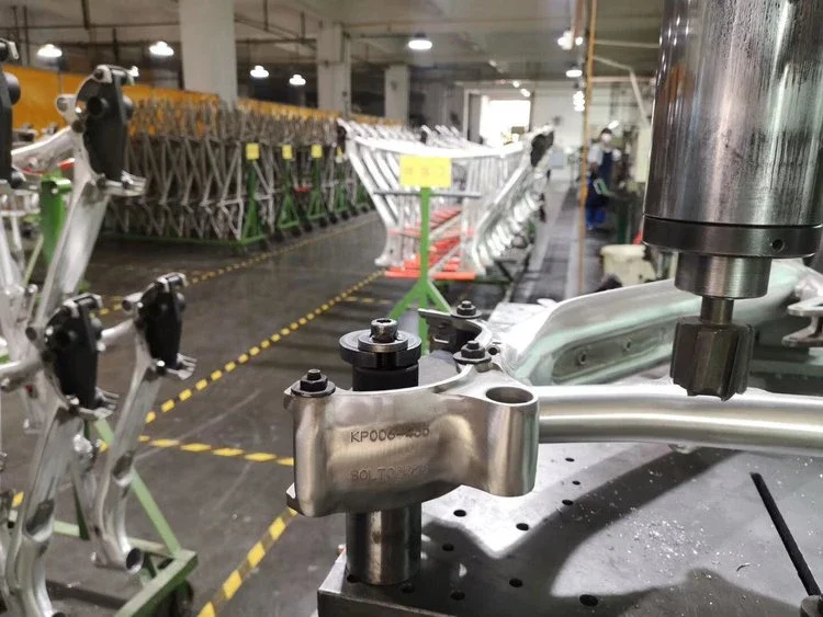 Close-up of machinery components on a production line in a manufacturing factory, with stacked metal parts in the background.