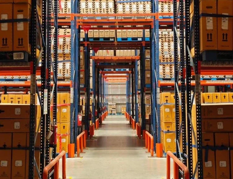Warehouse aisle with tall shelves stocked with cardboard boxes in organized rows.