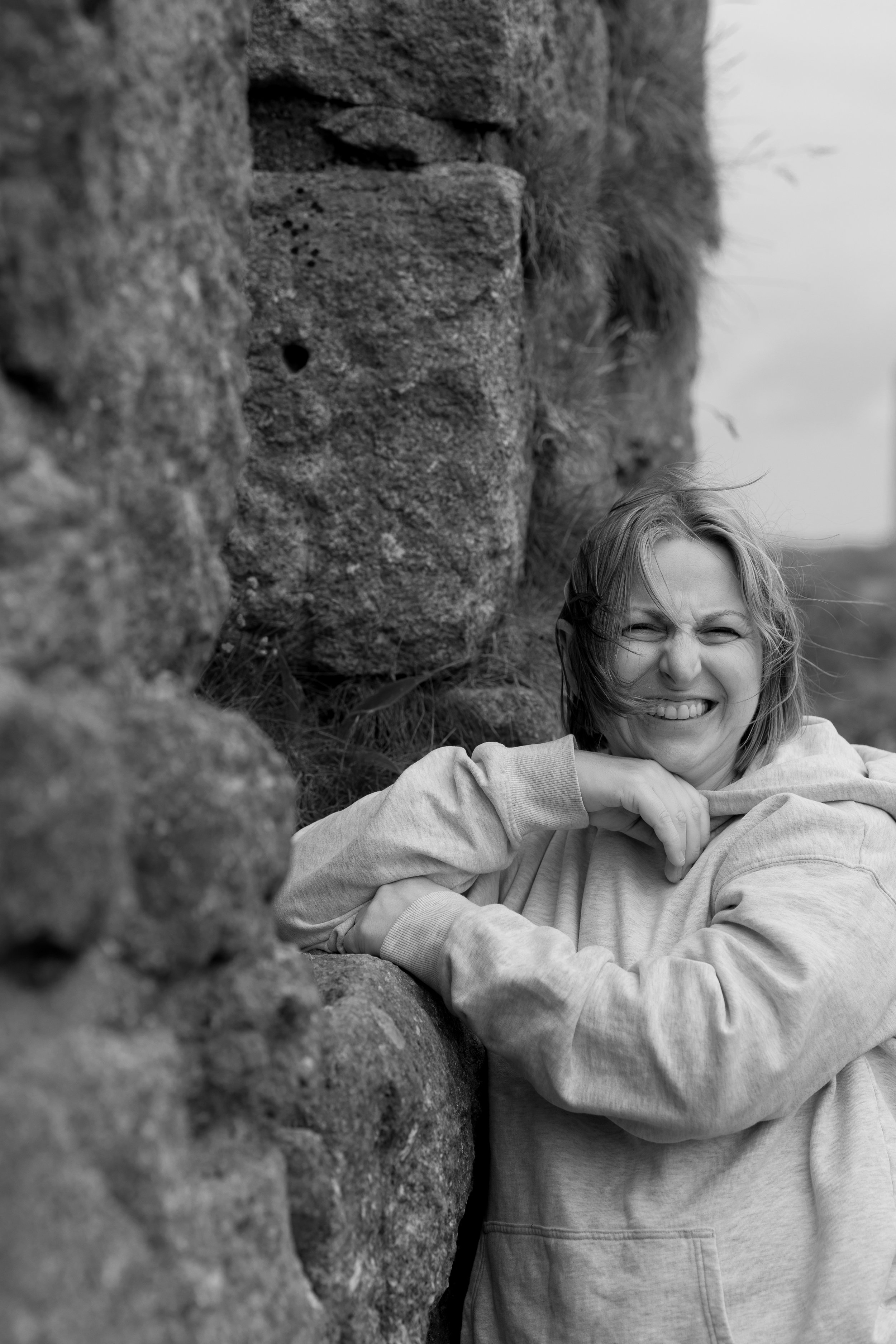 Susan Bradfield, photographer and visual artist. Blonde hair, smiling and squinting, leaning against a mine in Cornwall.