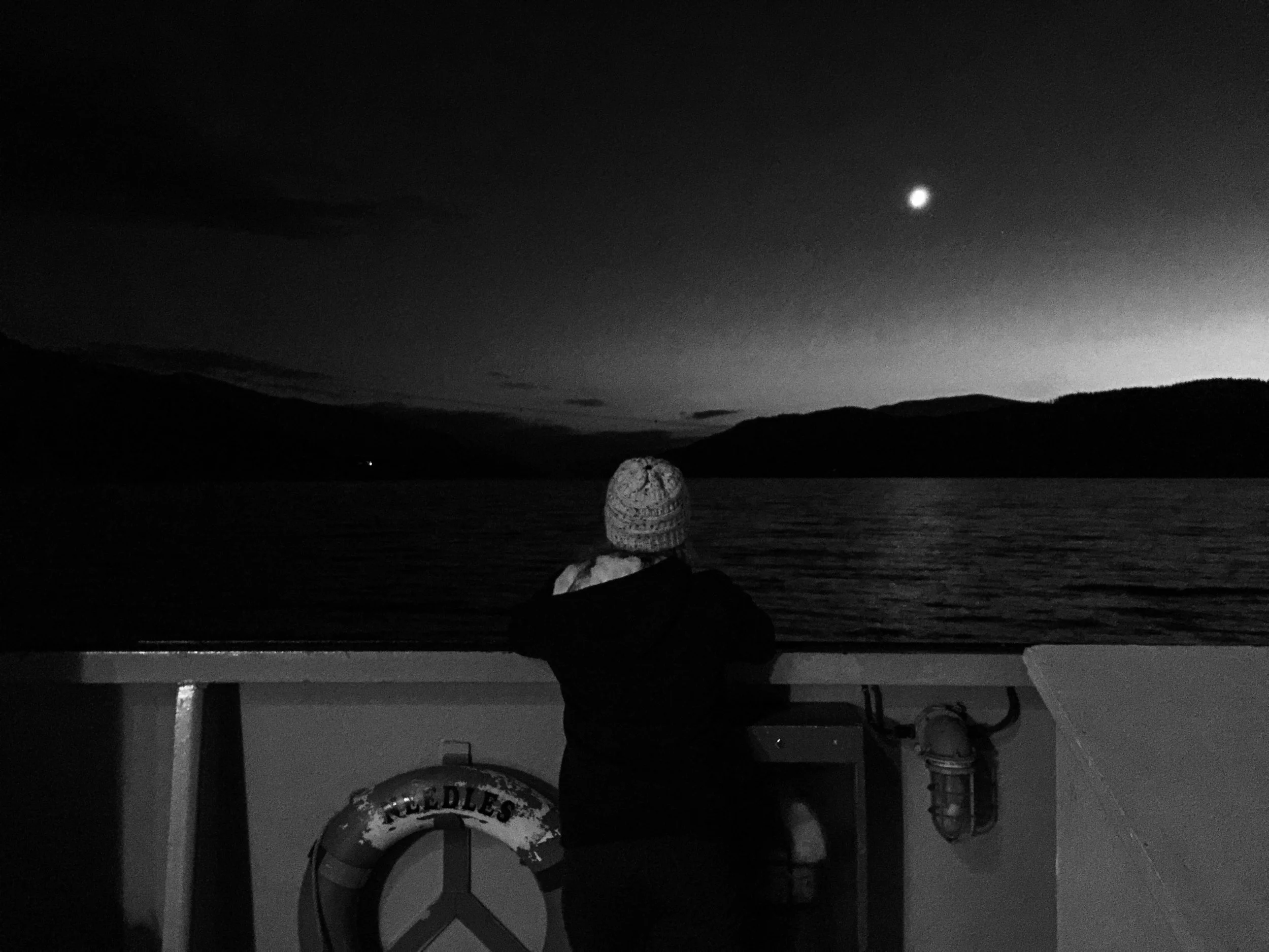 Melissa Lynn Sharp looking out over the ocean from the back of a ferry at night, symbolizing reflection, emotional resilience, and finding peace during difficult times.