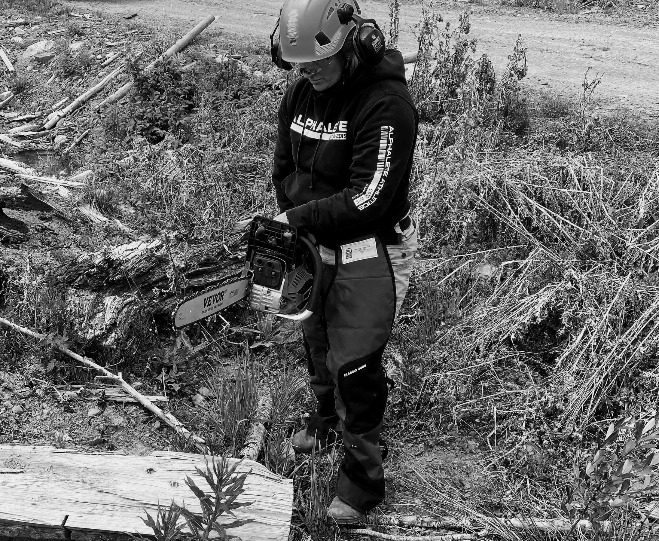 Melissa Lynn Sharp standing with a chainsaw in rugged terrain, representing resilience, capability, and finding strength during uncertain times.