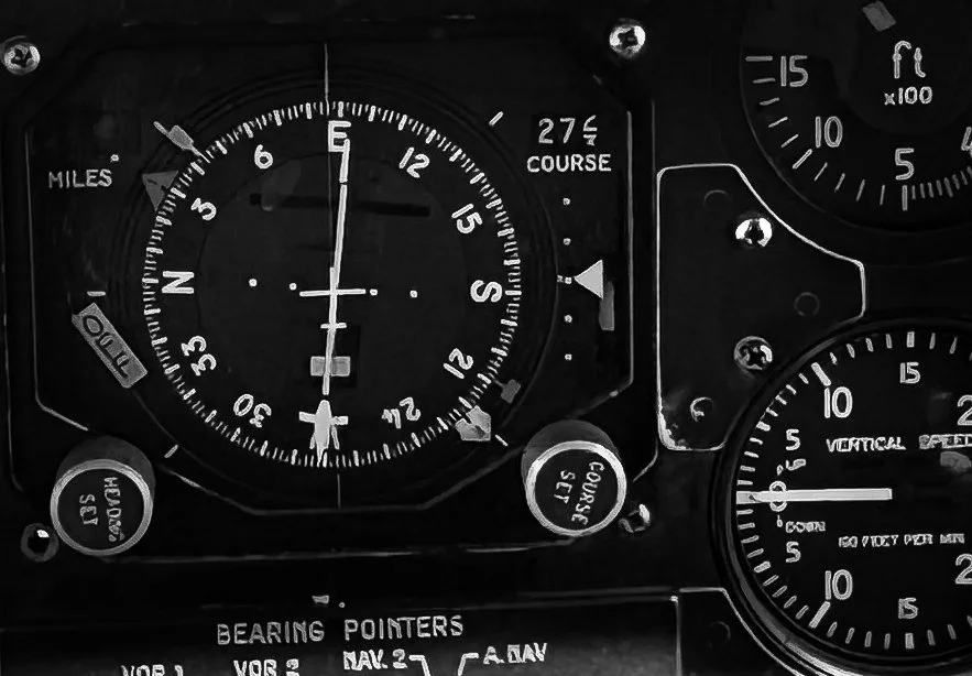 Black-and-white close-up of a course indicator and surrounding instruments on an aircraft cockpit panel.