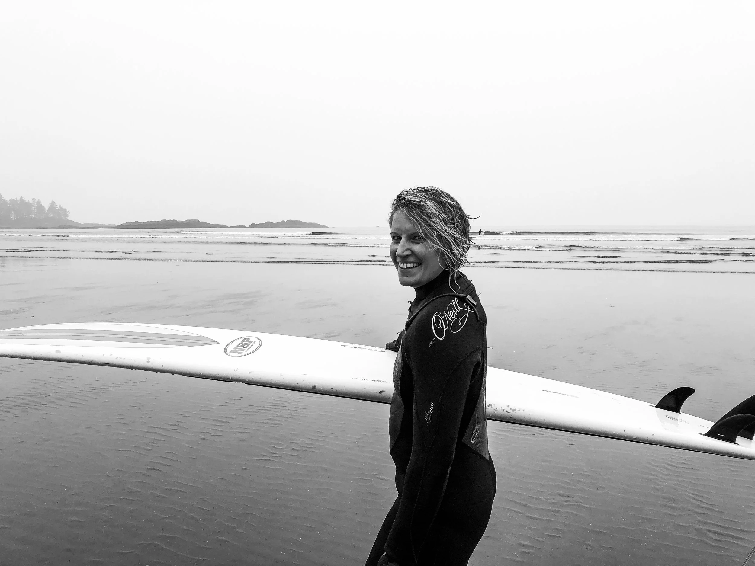Melissa Lynn Sharp carrying a surfboard along a beach in Tofino, symbolizing emotional resilience, courage, and learning to navigate life's challenges.