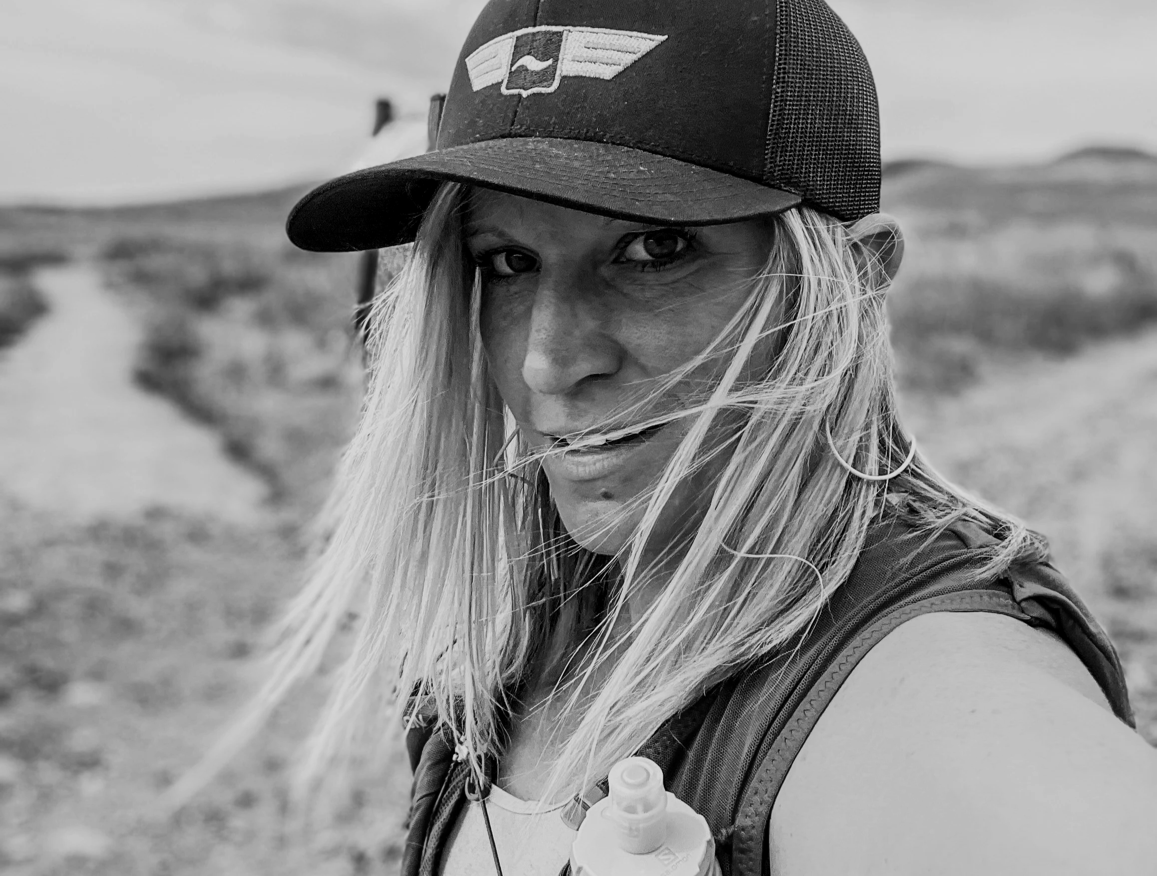 Melissa Lynn Sharp standing in the wilderness with wind blowing across her face, symbolizing resilience, vulnerability, and quiet inner strength.