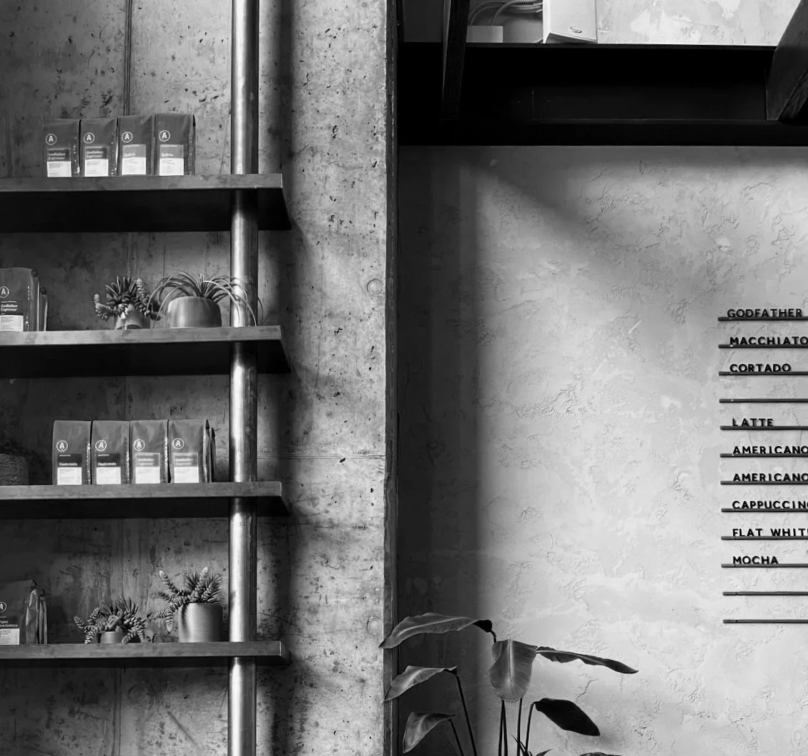 Concrete café wall with a metro-style menu and coffee bags, representing thoughtful decisions, community, and the energy exchanged through everyday interactions.