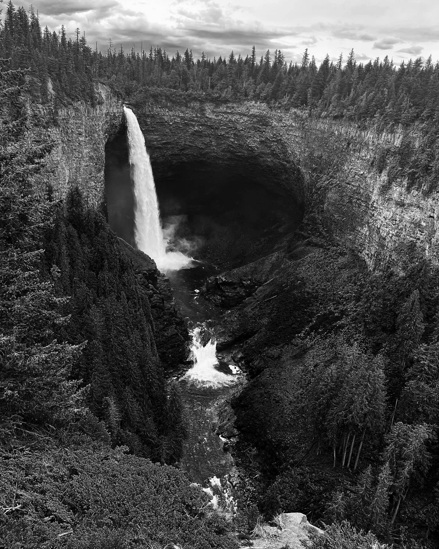Waterfall plunging into a deep forested canyon beneath a cloudy sky.