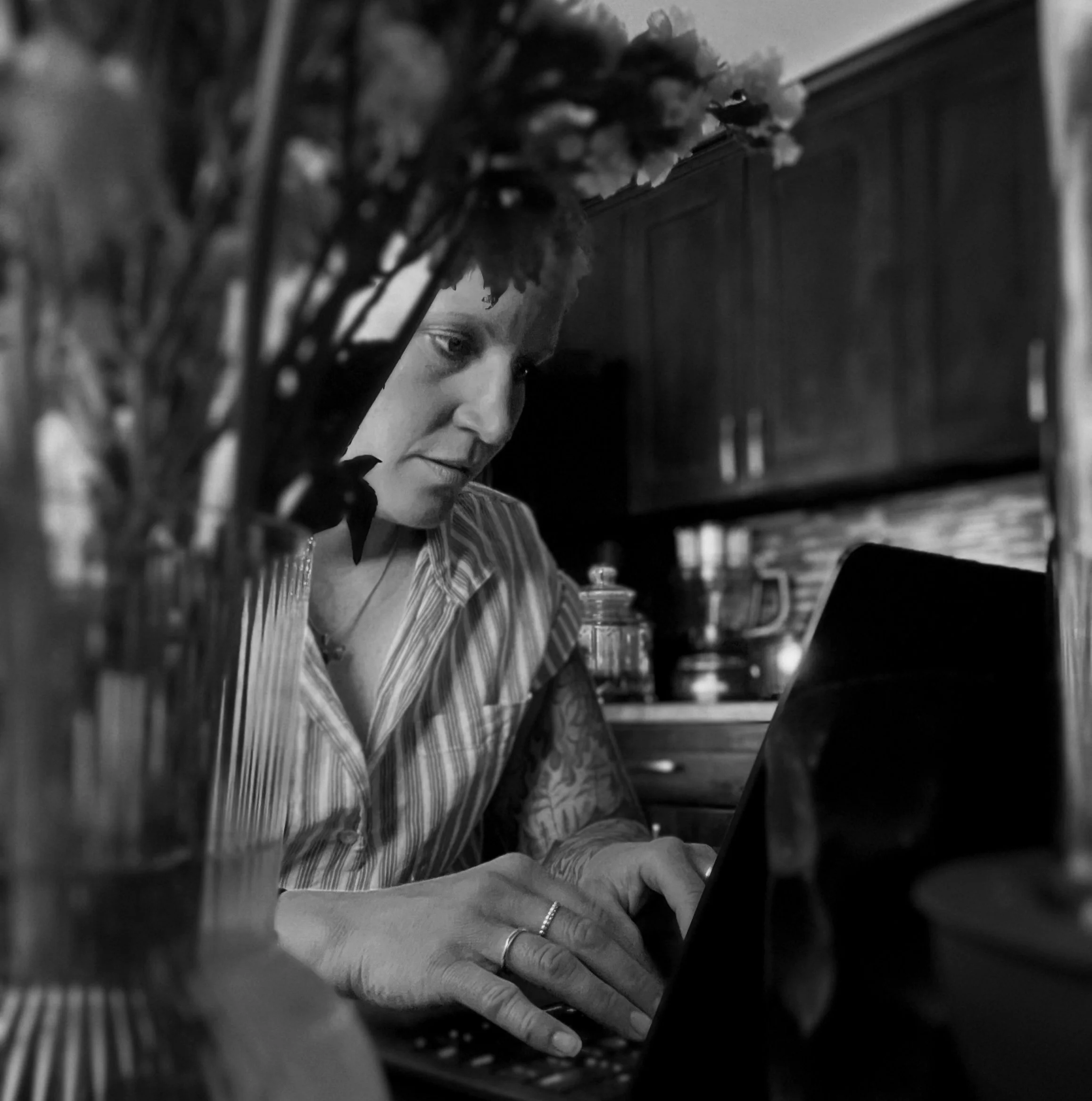 Melissa Lynn Sharp writing The Art of Being Human on a laptop while seated at a table surrounded by flowers.