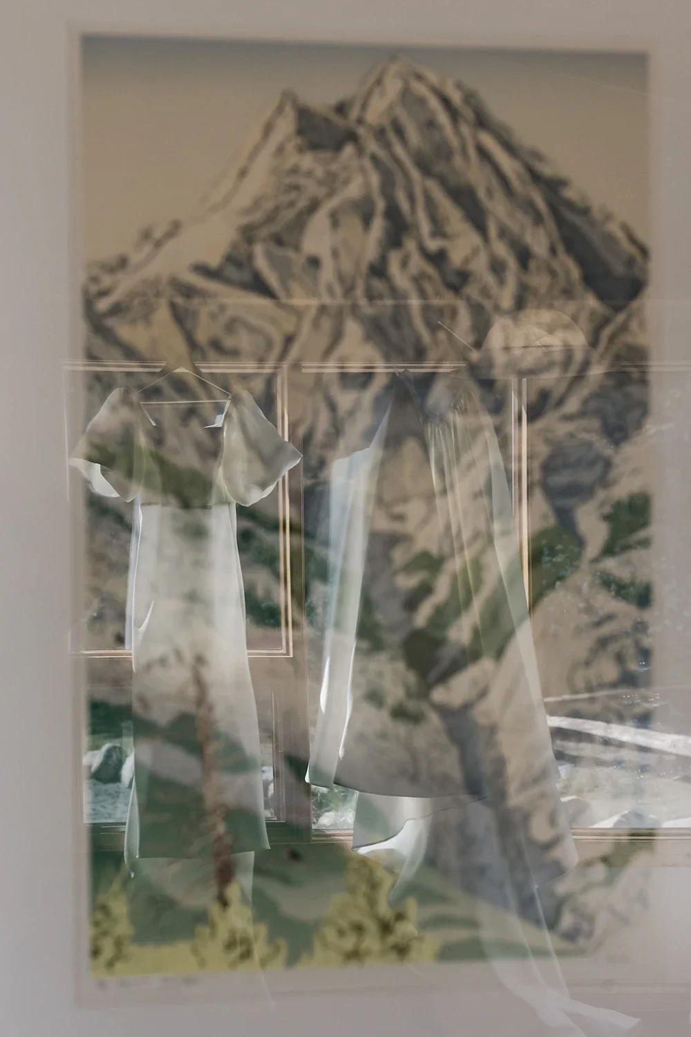 Reflection of a mountain landscape with a hanging white dress on a display stand.